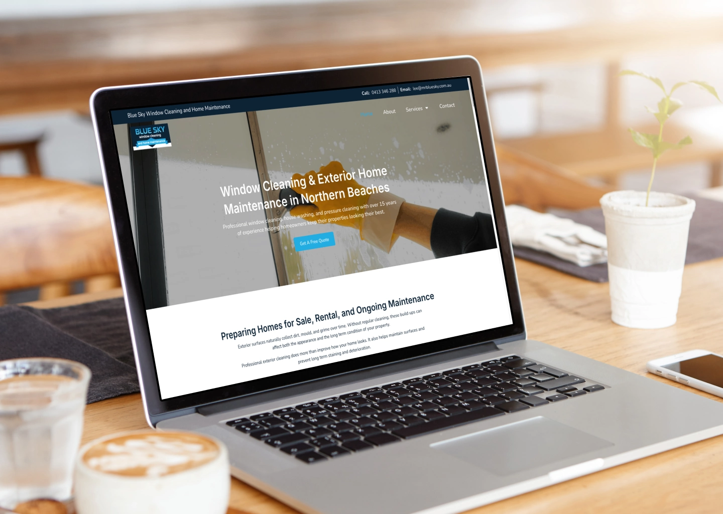 Laptop on a wooden table shows a window cleaning service homepage with a blue header and a 'Get a Free Quote' CTA.