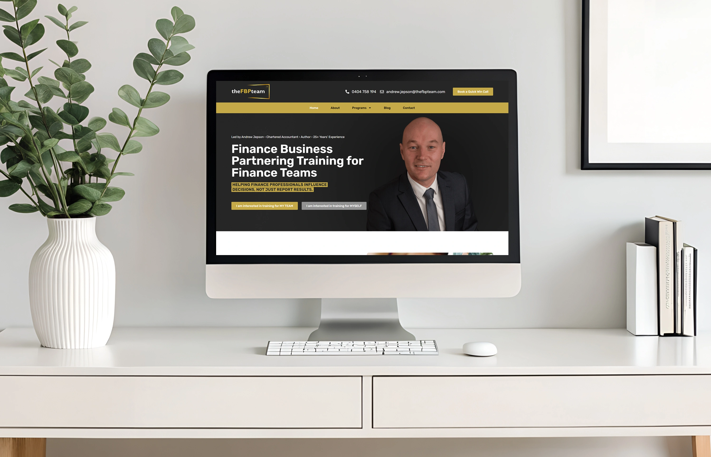 Desktop monitor on a white desk displaying a finance training webpage with a man in a suit on the right